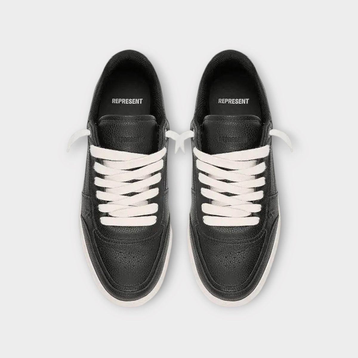 Drop Represent Initial black leather sneakers with white laces, top-down view of low-top athletic footwear.