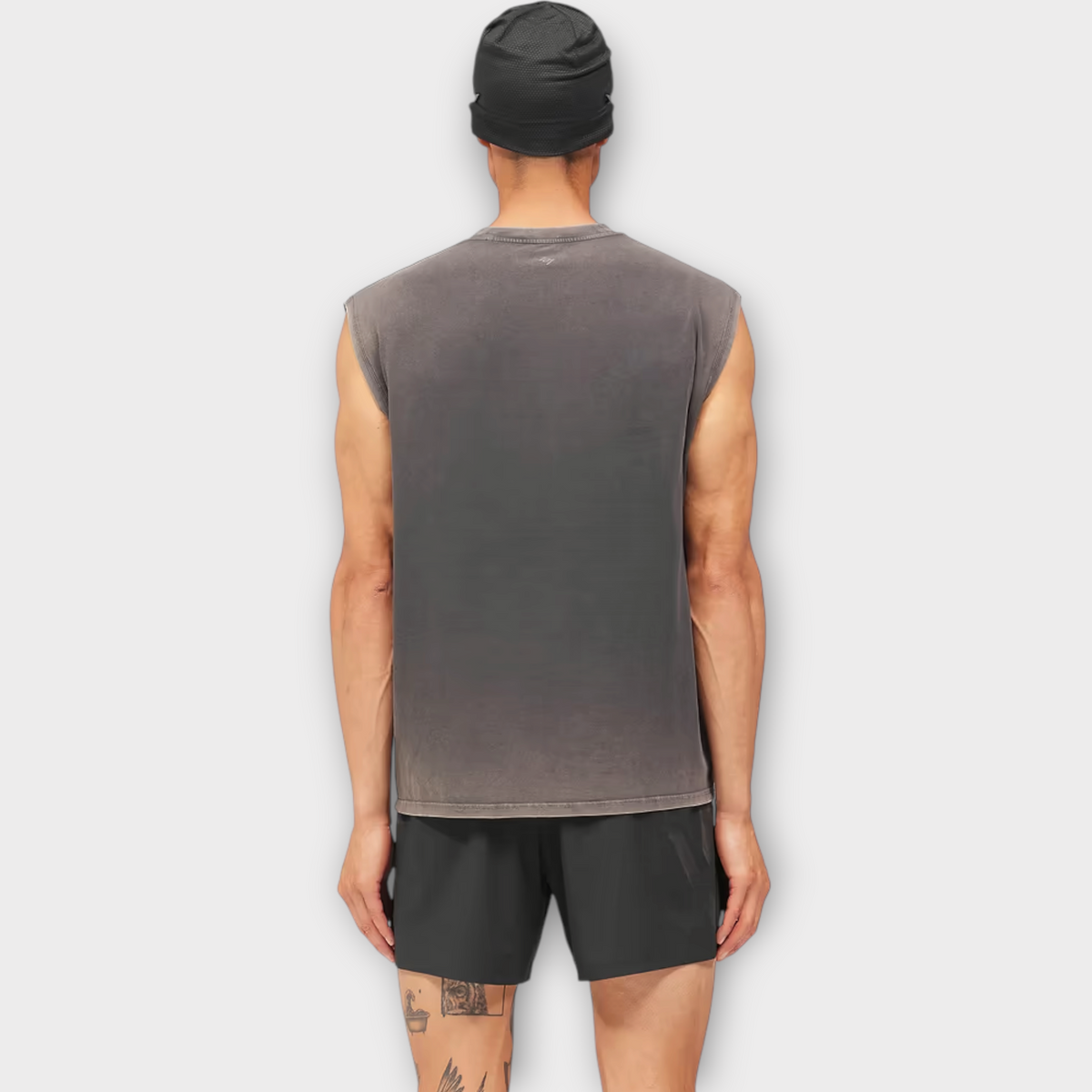 Back view of a man wearing a Drop 247 Angel graphic tank in vintage black with a black beanie and athletic shorts.