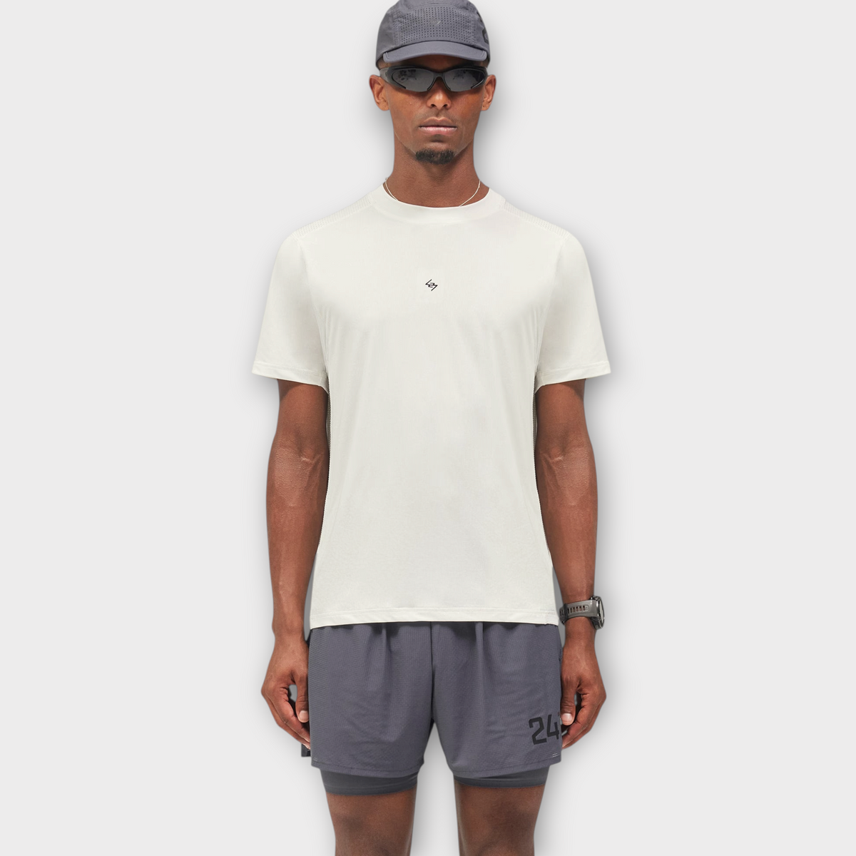 Drop model wearing a flat white 247 FW26 Numbers T-shirt with grey athletic shorts, cap, and sunglasses.