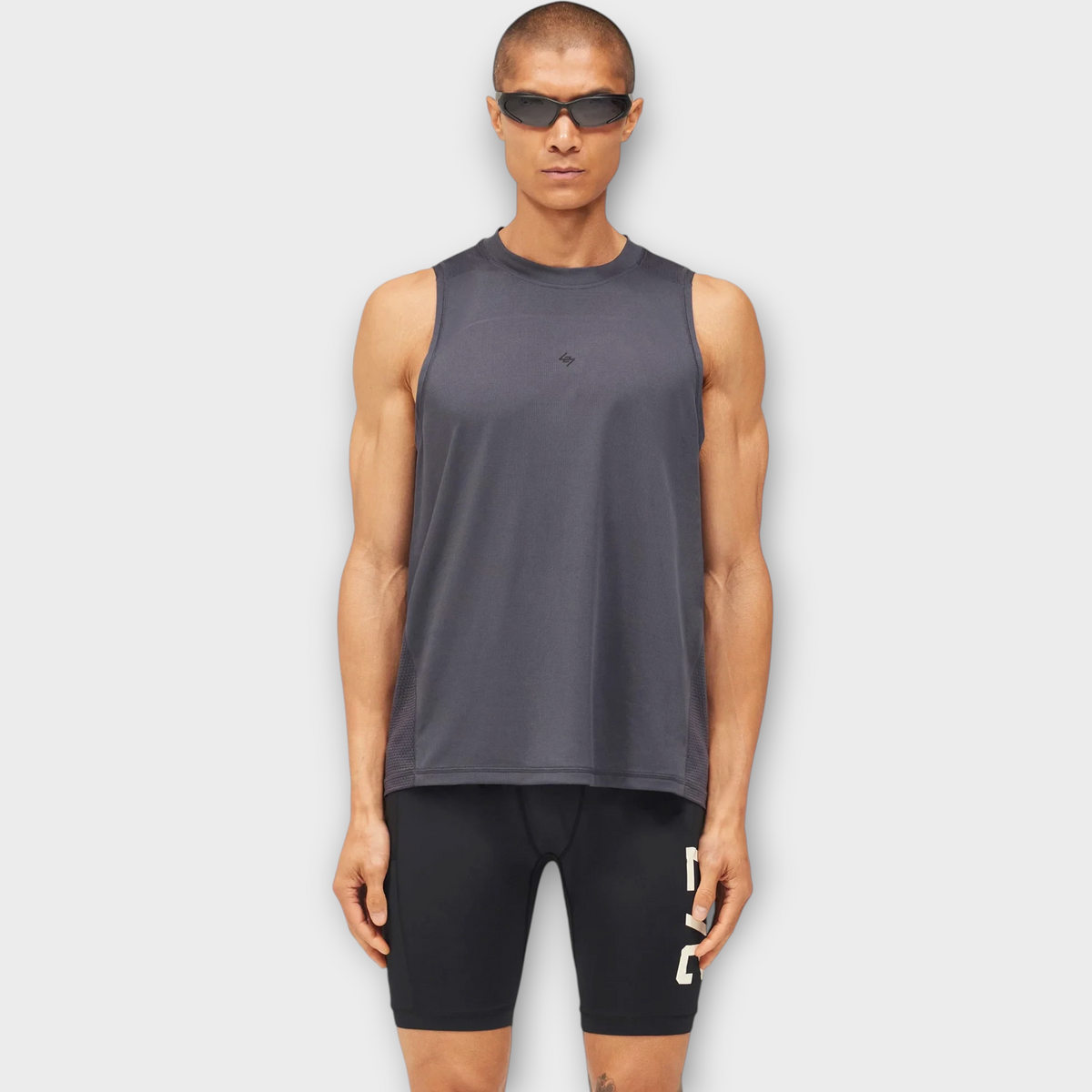 Drop 247 FW26 Numbers Vest in graphene grey worn by a model with sunglasses, featuring a sleeveless athletic design.