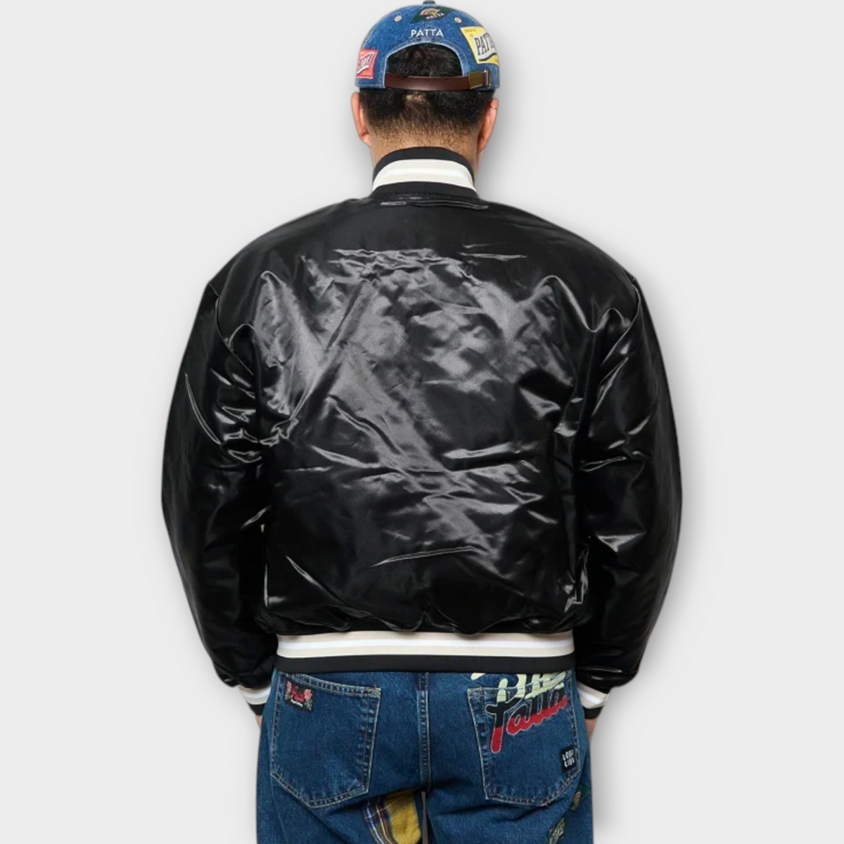 Drop Patta black satin varsity jacket with striped ribbed collar and cuffs, worn by a model from the back view