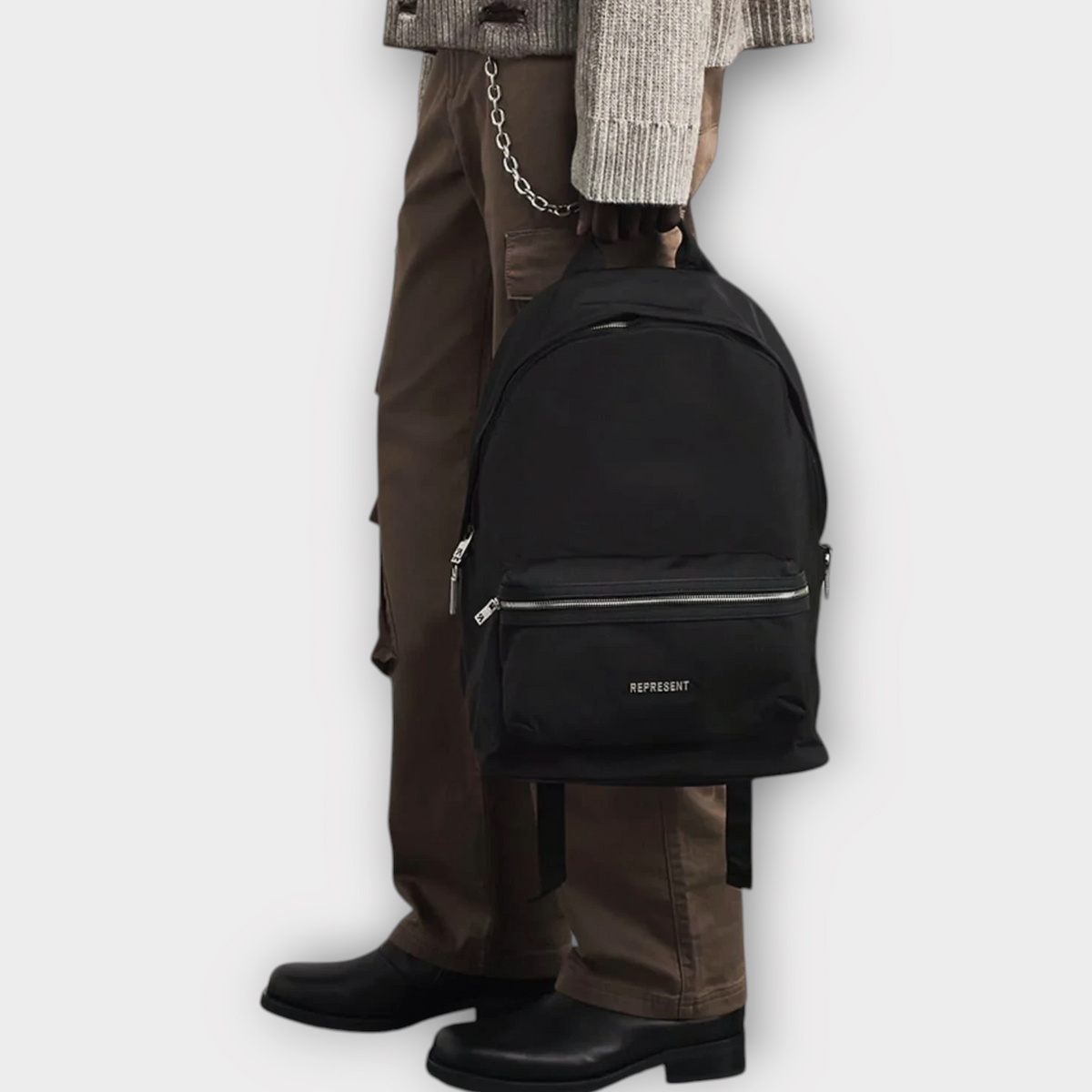 Drop Represent black nylon backpack held by a model wearing a distressed sweater and brown cargo pants