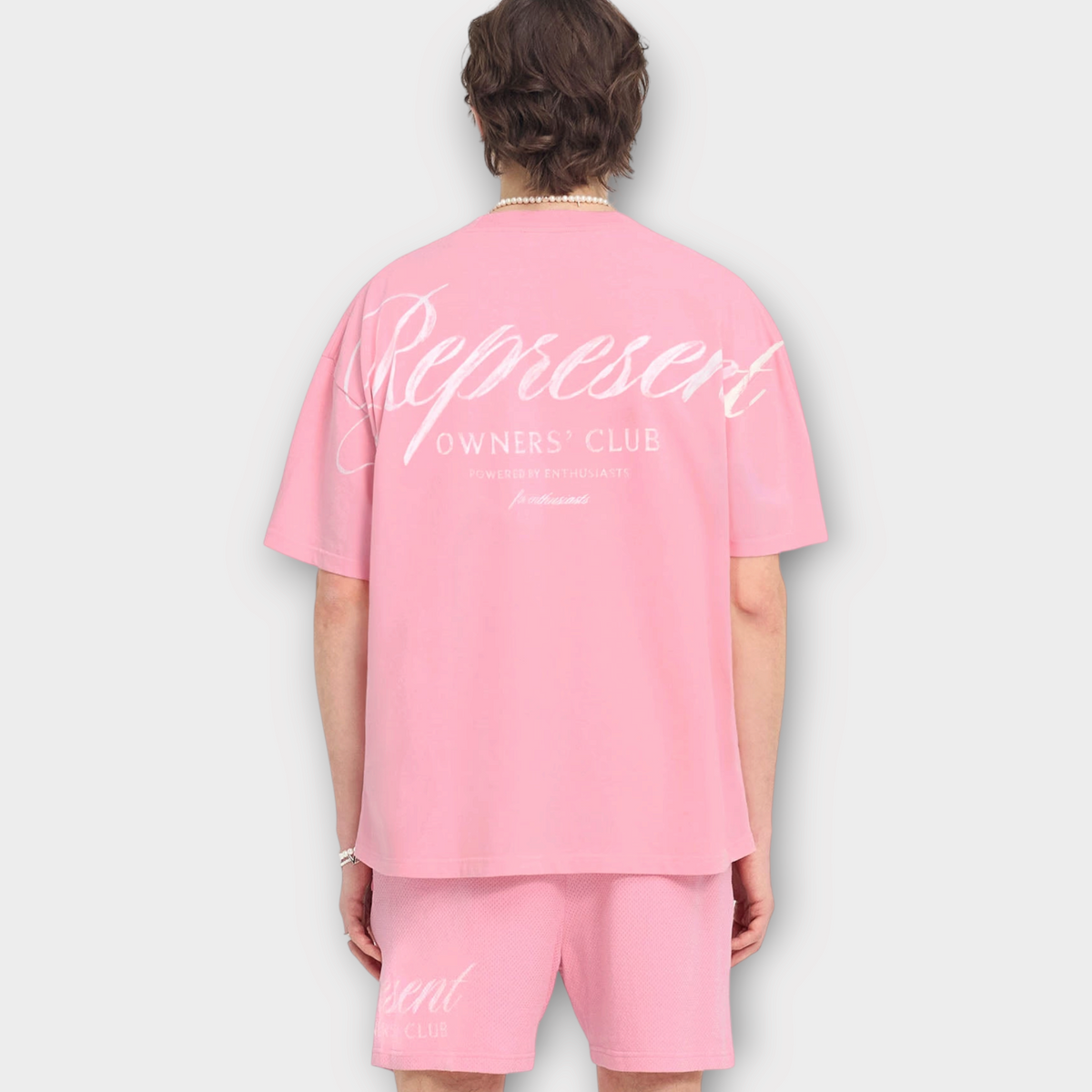 Drop Represent Owners Club pink t-shirt with white script logo on back worn by a man from behind